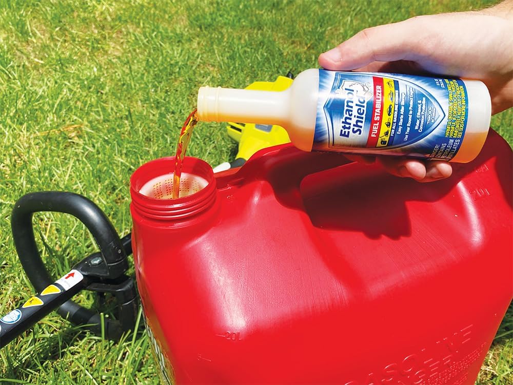 Pouring Ethanol Shield fuel stabilizer into a red gas can beside a string trimmer